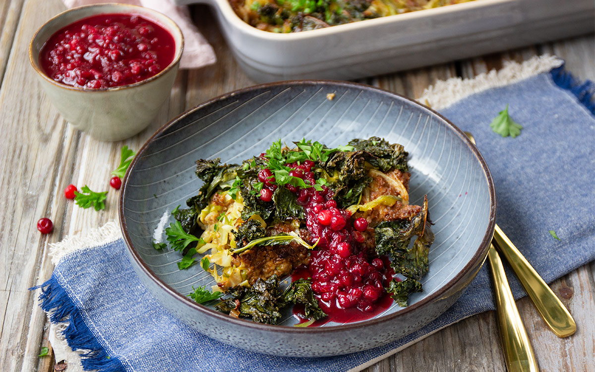 Tallrik med vegetarisk kålpudding med spetskål och grönkål toppad med lingonsås